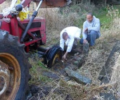 Anagarikas Laurence and Joe work to get the tractor wheel out of the creek