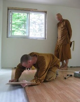 Samanera Sumangalo installs floor boards in the new kuti.  Is that a whip or a fly whisk in Ajahn Viradhammo's hand?